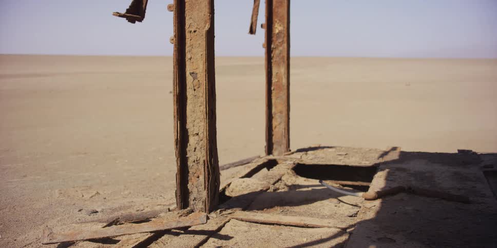 A close-up of a rusted and forgotten metal structure in the desert as wind blows sand across the desolate landscape
