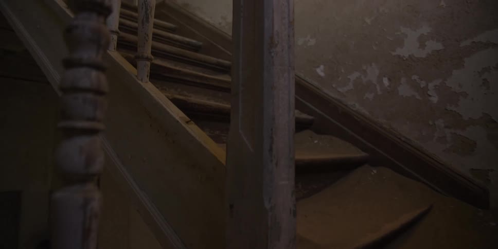 A slow reveal of a decaying wooden staircase filled with desert sand inside an abandoned ghost town house