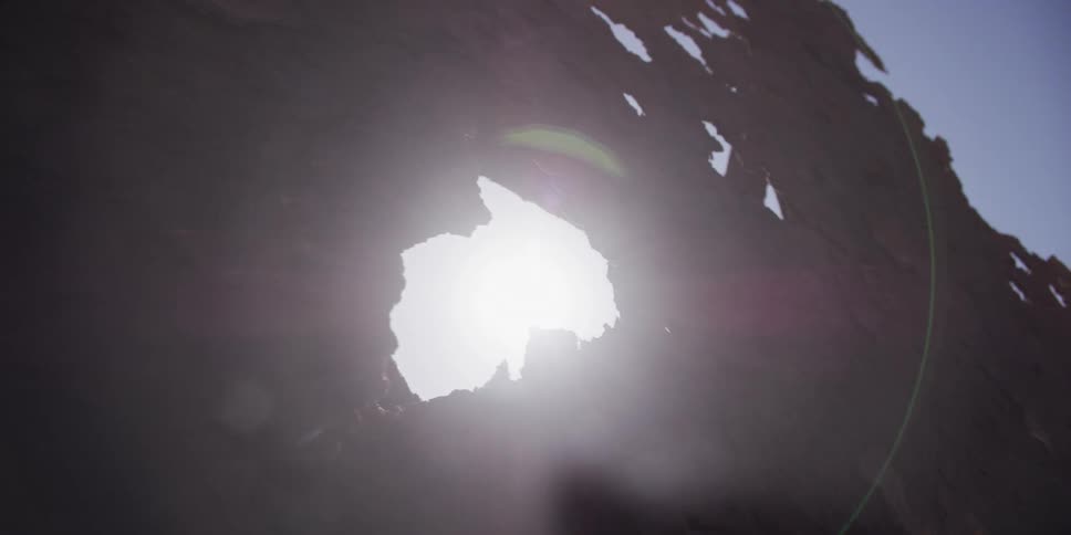 Sunlight dramatically flares through a hole in a silhouetted, decaying sheet of rusted metal