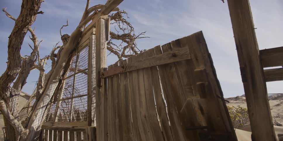 A slow push-in on the weathered and dilapidated wooden ruins of an abandoned desert shack