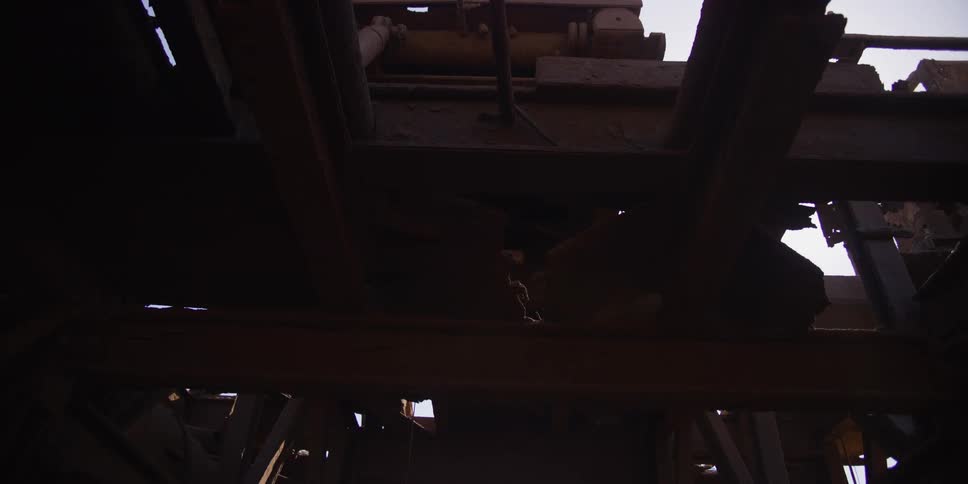 A slow pull-back shot reveals the dark, dilapidated, and rusty interior of an abandoned industrial structure looking up towards the sky