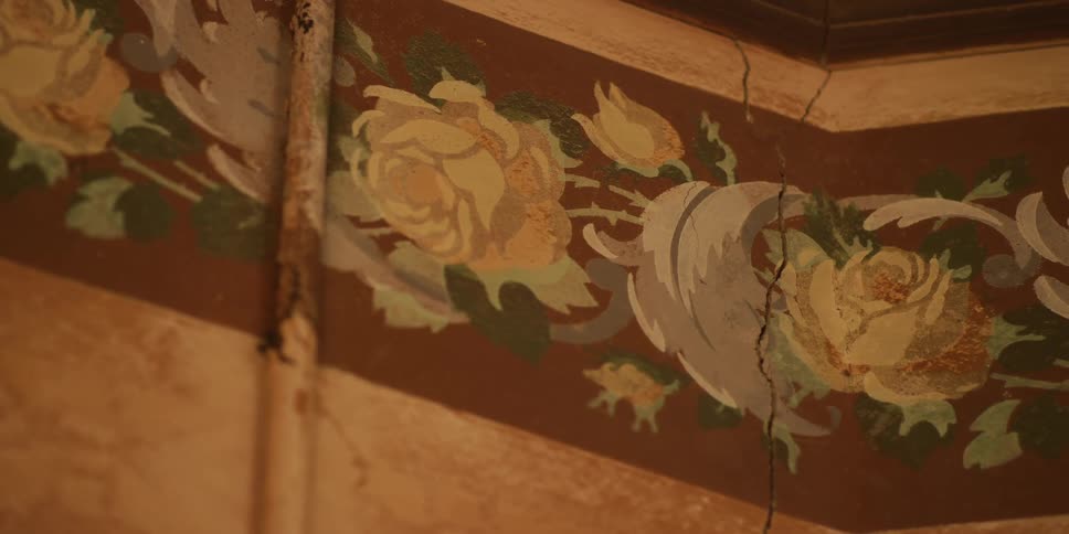 Close-up slow pan of a vintage, hand-painted floral border with yellow roses on a cracked and decaying wall