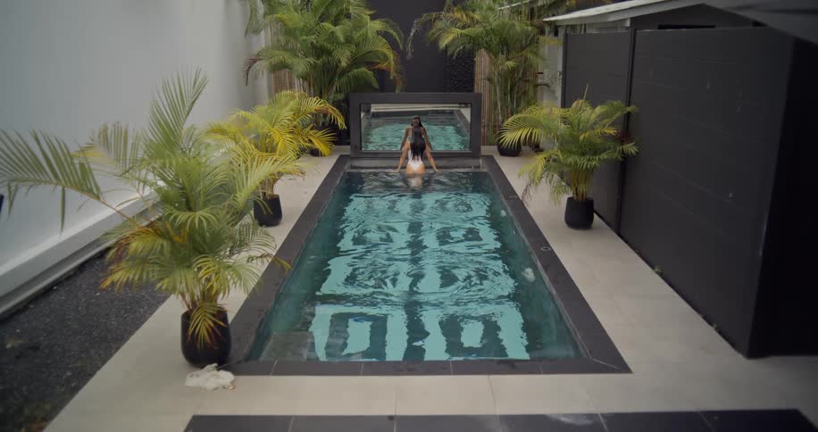 A couple enjoys a leisurely swim together in a luxurious and modern backyard pool at a tropical villa
