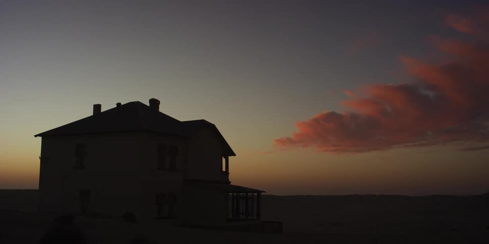 A timelapse shows the sunset and clouds changing color over an abandoned house in the Namibian desert