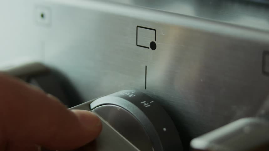 A person turns the knob on a metal stove