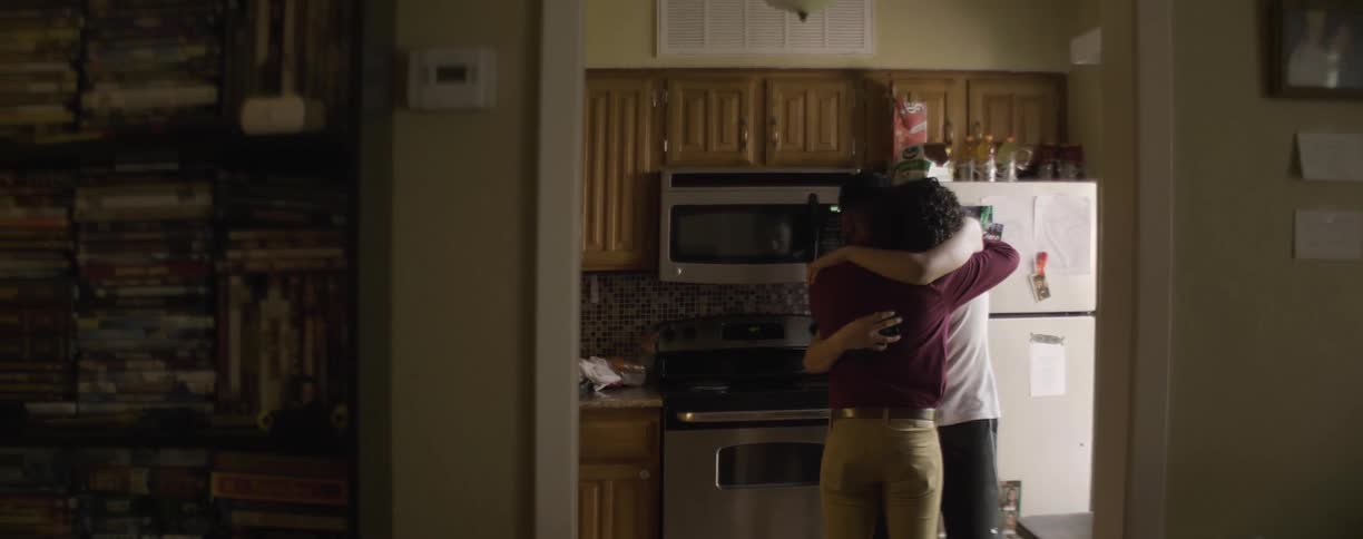 A man is crying as he holds onto another man in a kitchen