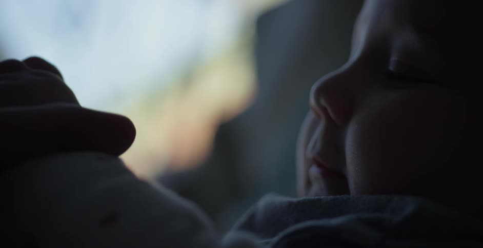 An infant uses both hands to hold onto an adult's fingers