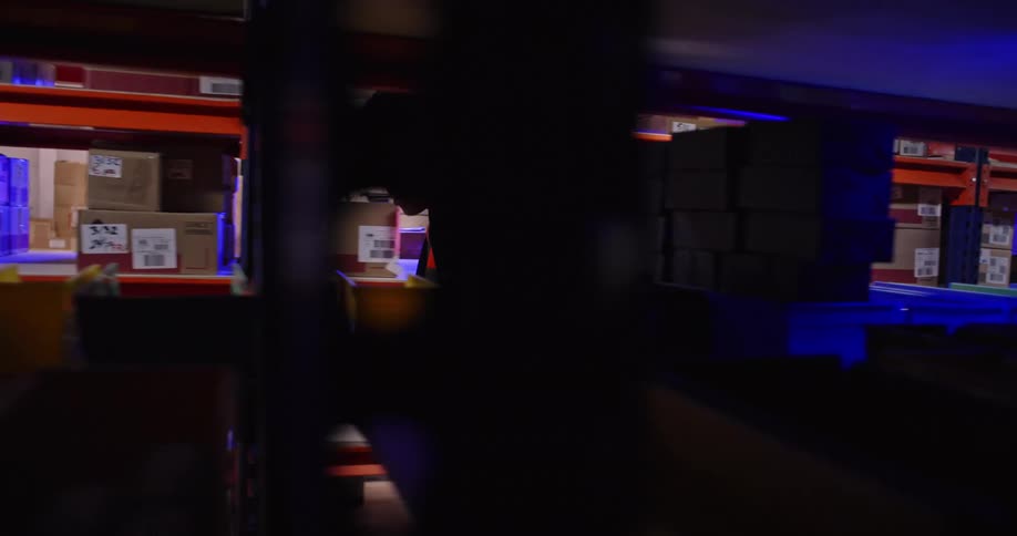 In a slow-motion tracking shot, a young warehouse worker in a high-visibility vest diligently searches for items in sorting bins