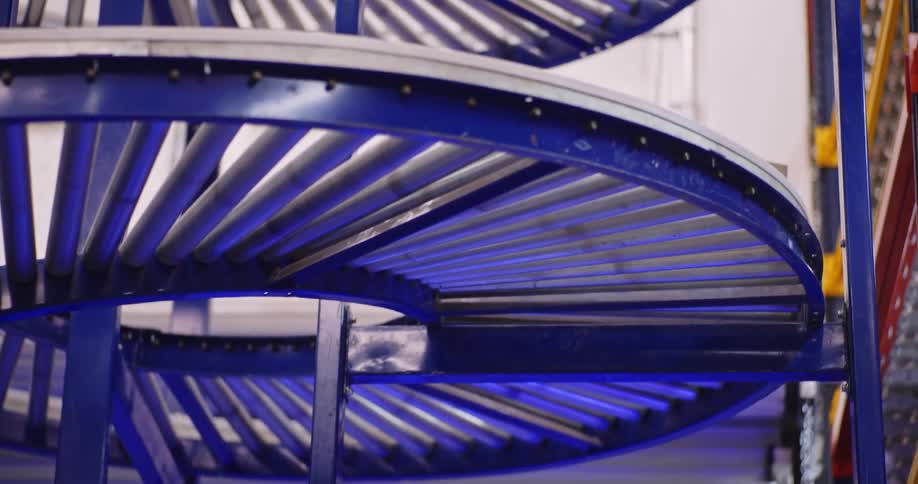 A cardboard box smoothly descends a multi-tiered spiral roller conveyor system inside a modern logistics warehouse
