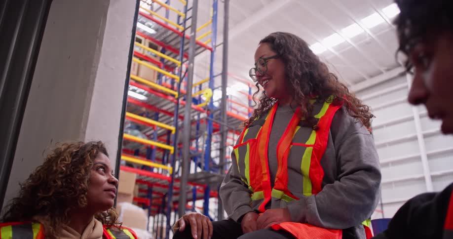 A diverse team of warehouse employees enjoys a lighthearted moment, laughing and chatting together during their work break
