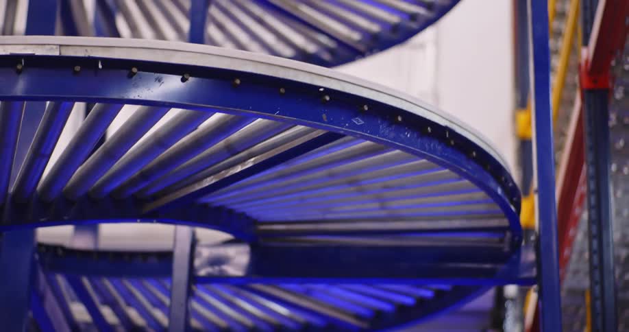 A single cardboard package glides down a spiral gravity roller conveyor in a modern logistics warehouse
