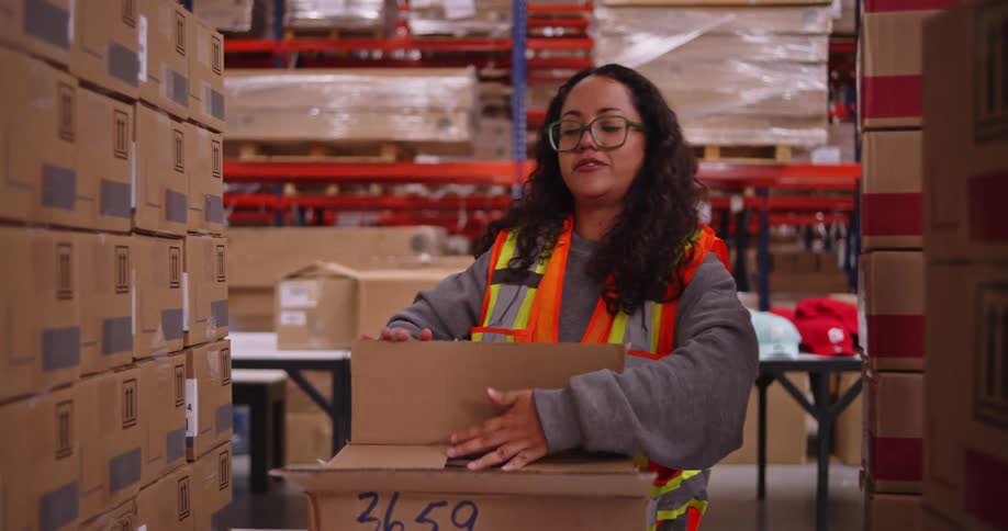 A warehouse worker photographs the contents of a package with her smartphone and then closes the box for shipping