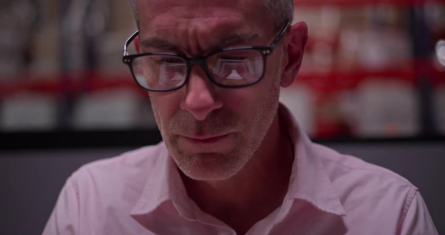 A middle-aged professional with glasses focuses intently on a screen, his expression a mix of concentration and deep contemplation