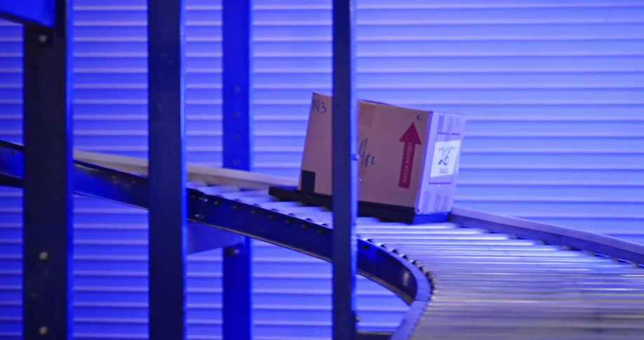 A single cardboard package labeled 'fragile' moves along a spiral roller conveyor belt system in a logistics warehouse