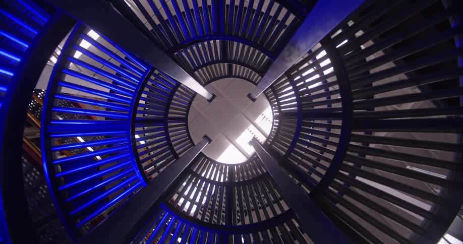 A low-angle, abstract view of a blue-lit, circular industrial machine rotating in a continuous loop