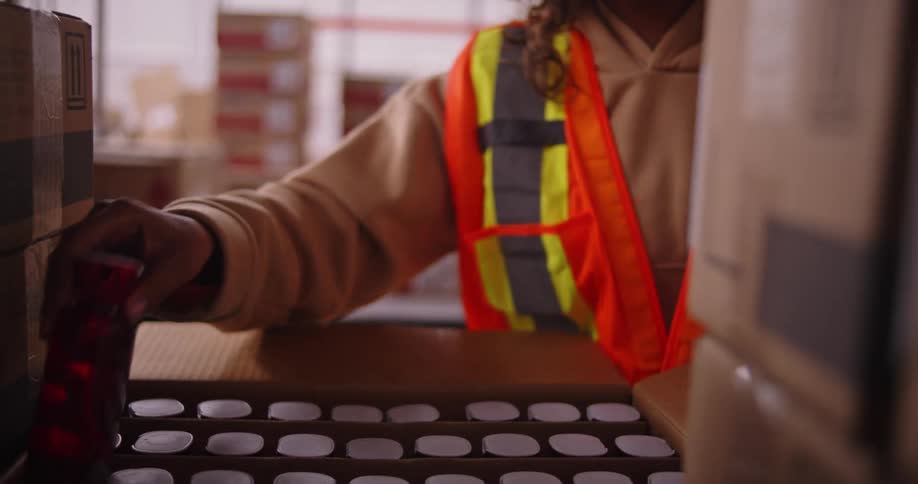 A female warehouse employee carefully inspects and packs a red water bottle into a shipping box on a production line