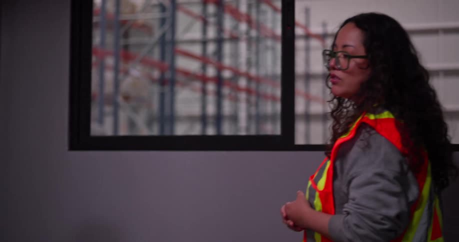 A male manager and a female warehouse worker in a safety vest have a focused meeting in a warehouse office