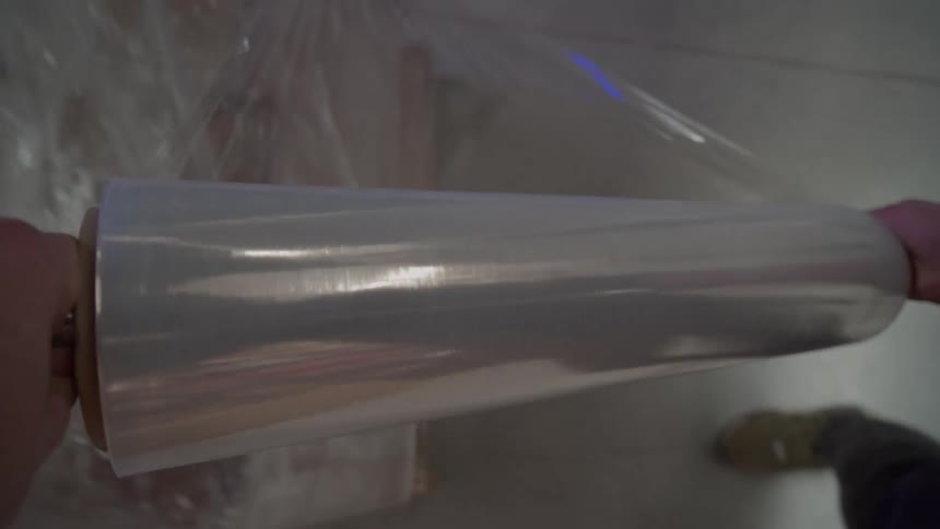 A first-person point of view shot of a worker wrapping pallets with plastic stretch film in a large warehouse