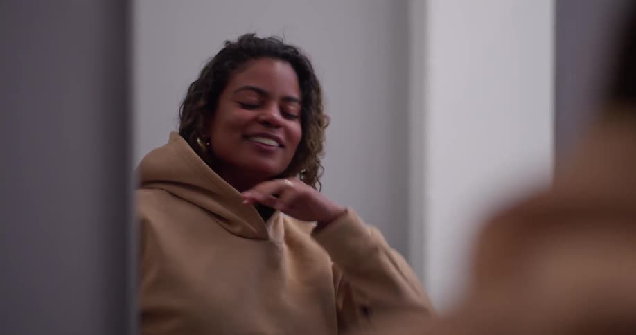 Slow motion shot of a young woman smiling and putting on her hoodie while talking with a friend in a locker room