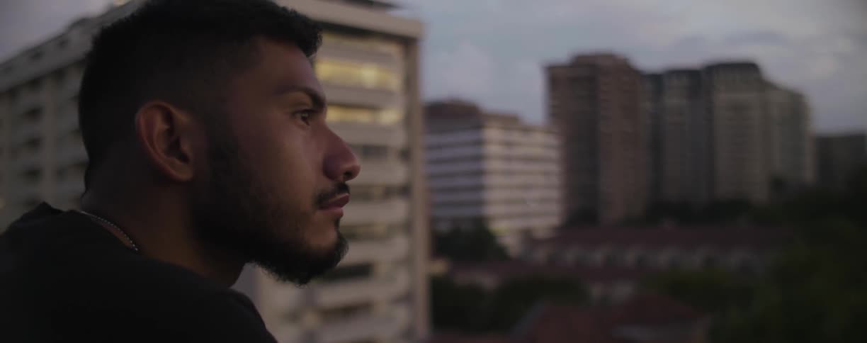 Sad man standing on balcony looks out towards city deep in thought
