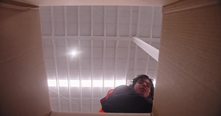 Warehouse worker carefully packs red water bottles into a cardboard box, viewed from the inside looking up