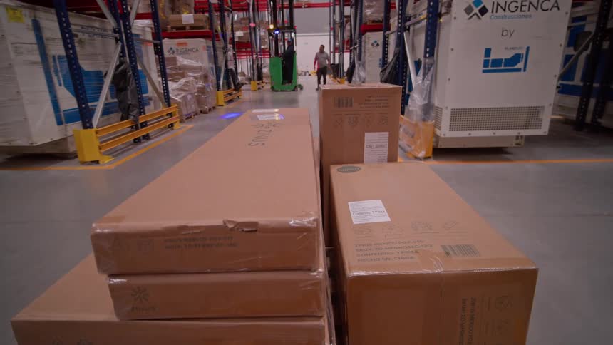 Slow zoom out shot of packages in a distribution warehouse as a forklift and workers move down the aisle