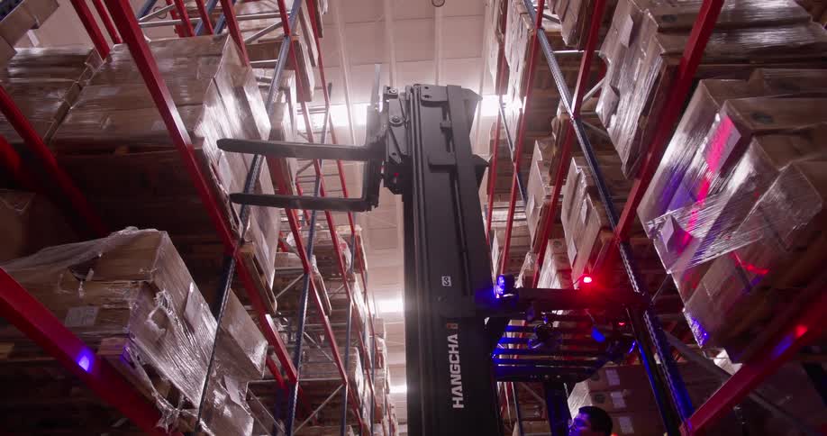 A forklift operator elevates the lift to reach the top shelves of a towering warehouse storage rack