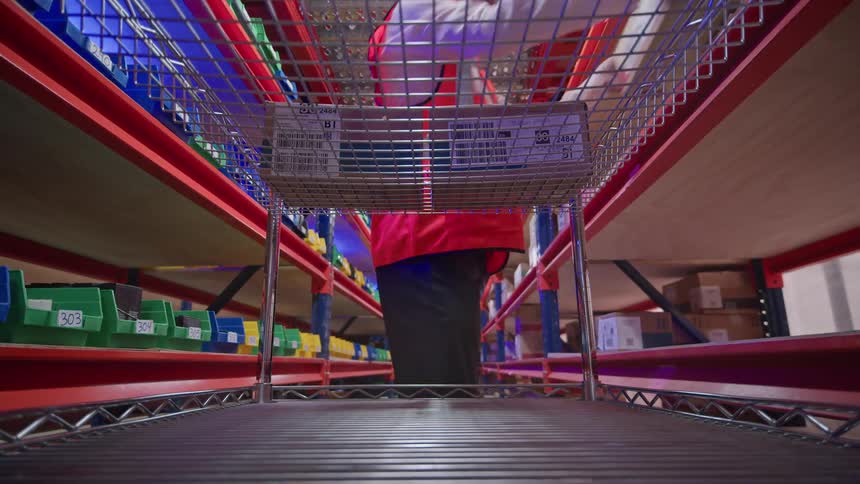 A point-of-view shot from inside a rolling cart as a warehouse worker loads it with boxes from the shelves