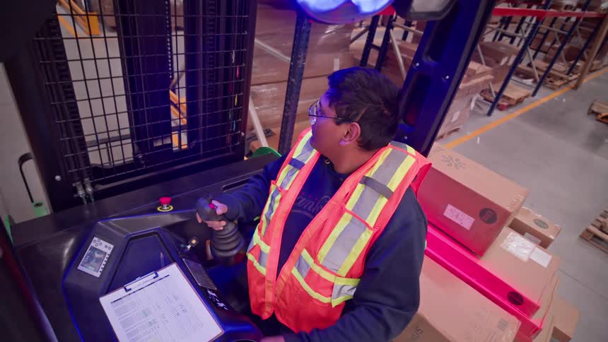 High-angle point-of-view of a warehouse worker operating a forklift, creating a motion blur effect as he moves through the aisles
