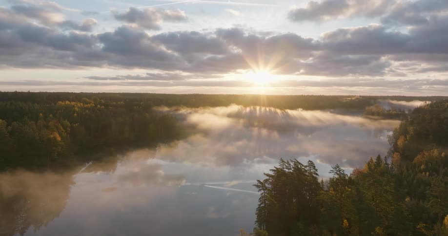 A glorious sunrise sends beautiful sun rays over a misty lake surrounded by a vast autumn forest