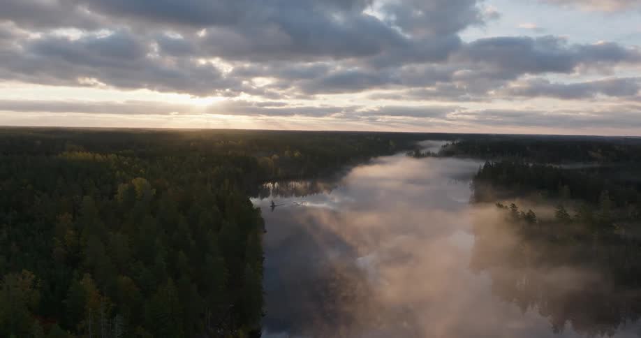 A majestic aerial view captures the sunrise breaking through clouds over a misty river winding through a vast forest