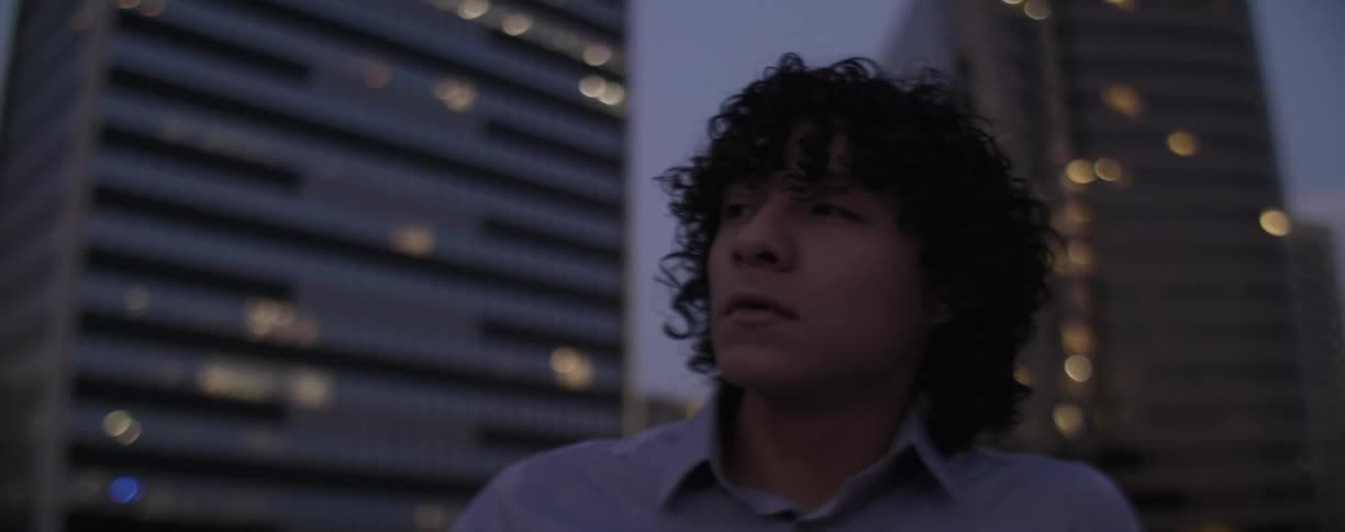 A young man sits in contemplation outside in an urban setting at dusk