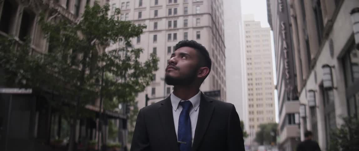 A man stands on a city street and looks up at the tall buildings