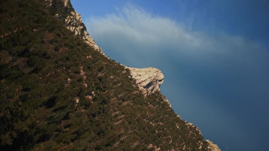 A dramatic shot of a tree-covered mountain peak rotates slowly from a landscape to a vertical orientation