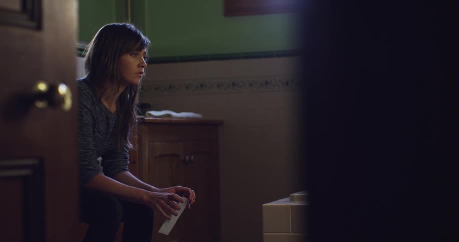 Woman sits in bathroom with a closed letter in her hands
