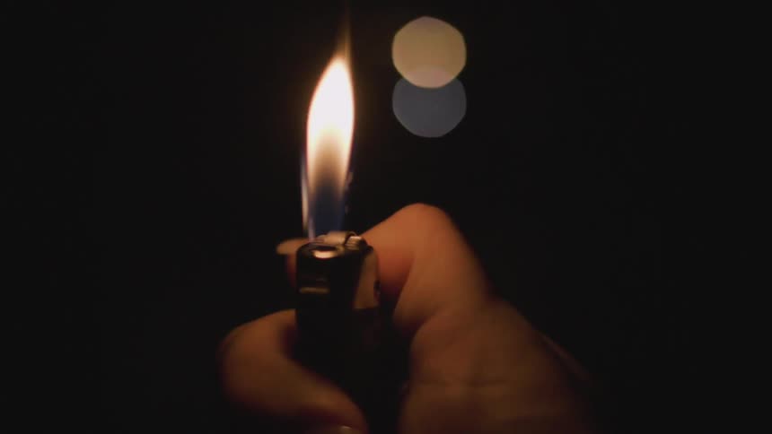 Hand ignites a lighter in the dark