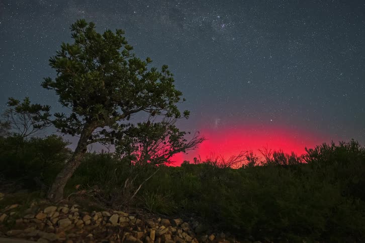 A stunning night timelapse shows the starry sky and Milky Way moving over a vibrant red glow from a distant volcano or large fire