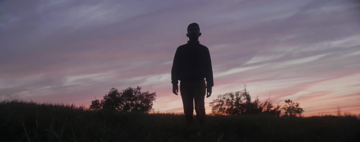 Man walks down a grassy hill at sunset