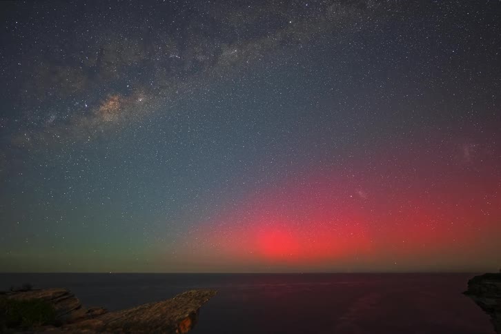 A stunning timelapse captures the vibrant red glow of the Aurora Australis and the Milky Way galaxy in the night sky over the ocean