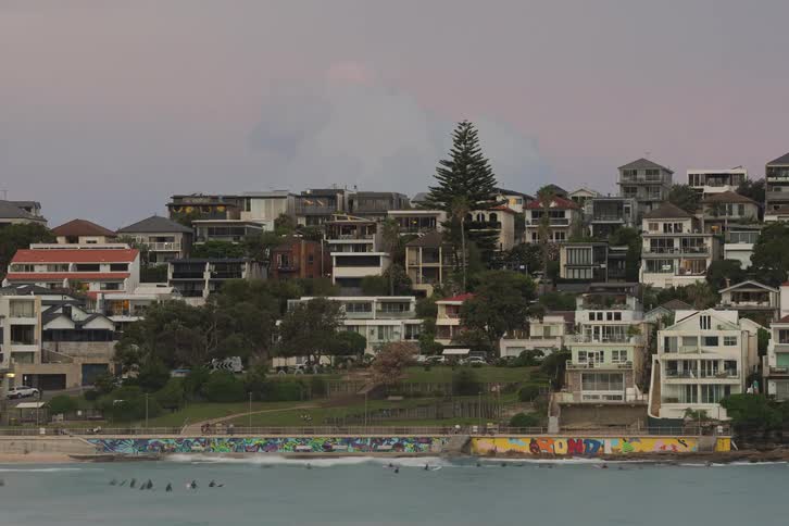 A time-lapse of surfers at Bondi Beach in Sydney, Australia as sunset clouds move over the hillside homes and graffiti seawall