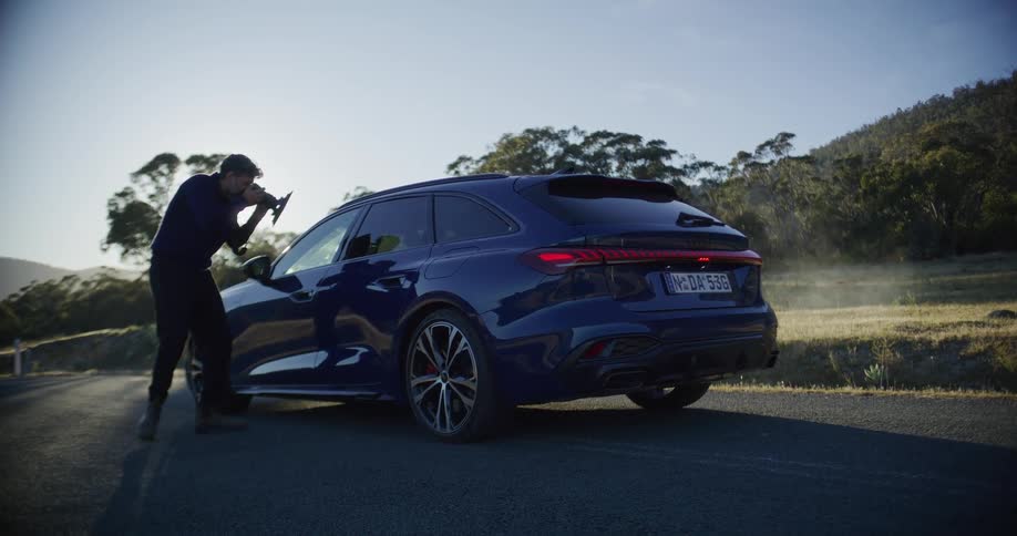 A professional photographer captures images of a luxury blue station wagon on a scenic country road at sunrise