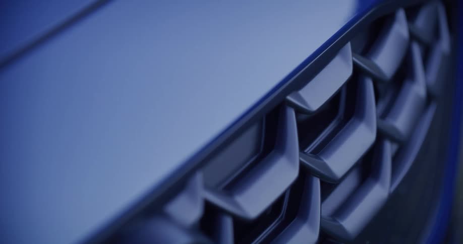 A sleek, cinematic close-up of a modern blue car's front grille reveals its intricate design