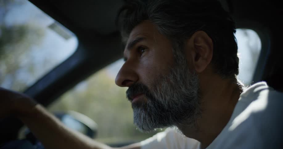 Close-up slow-motion profile of a distinguished bearded man driving a car on a sunny day