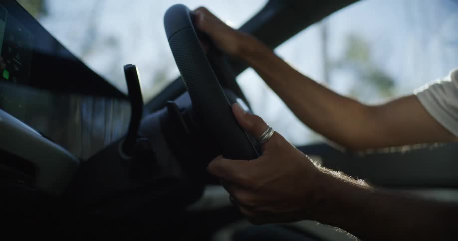 Sunlight streams through the car windshield, creating lens flare over a driver's hands gripping the steering wheel
