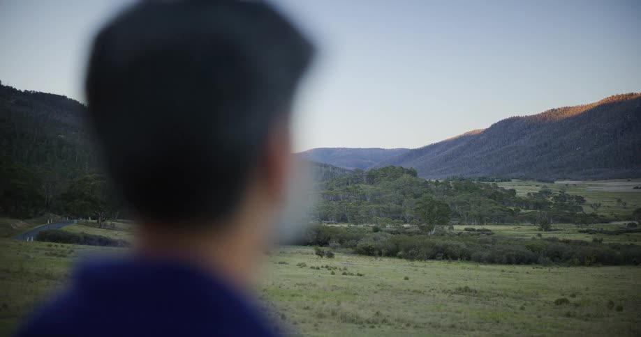 A male photographer in the foreground frames a shot of a beautiful, expansive valley with rolling hills at sunrise