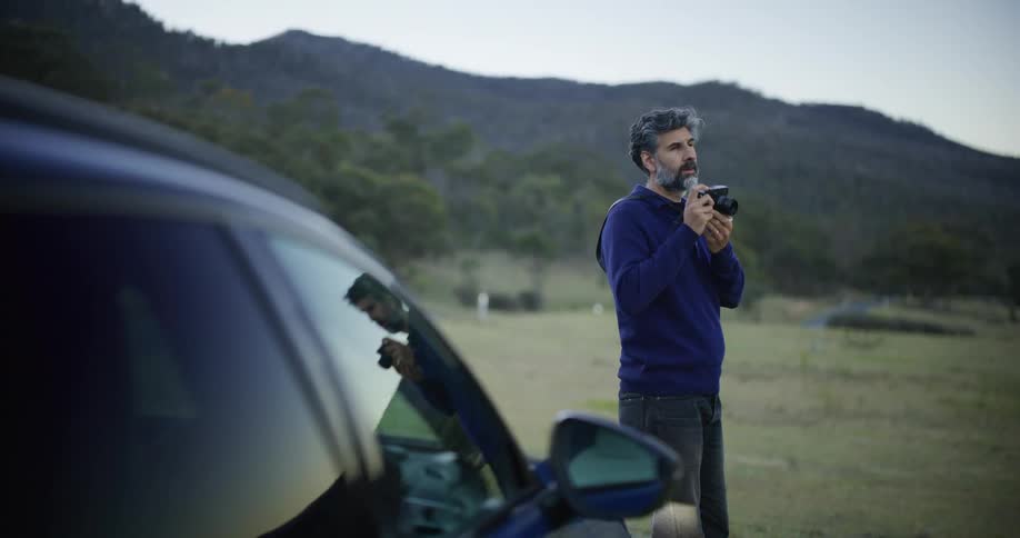 A handsome man on a road trip stops to take photos of the scenic mountain landscape at dusk