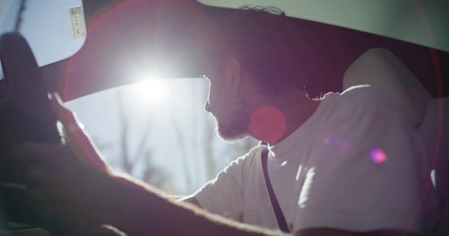 Side profile of a man driving through a sunlit road, with light and shadows playing across his face