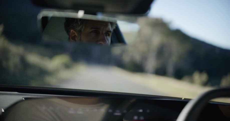 Slow motion shot of a man's eyes in the rearview mirror as he drives on a scenic road