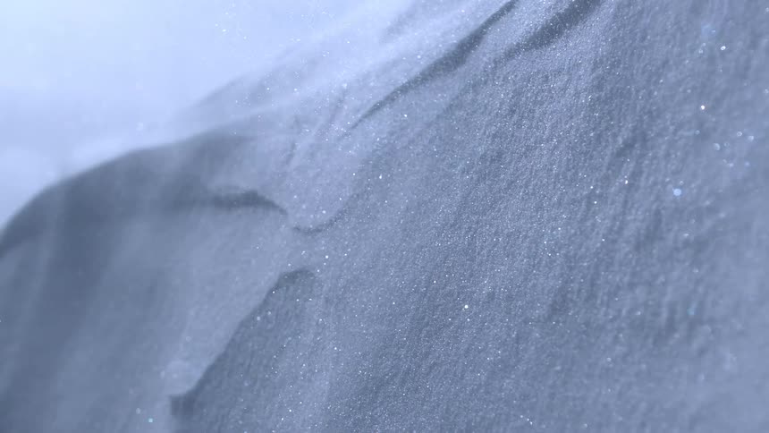 Wind blows tiny sparkling snowflakes across a fresh snowdrift in slow motion