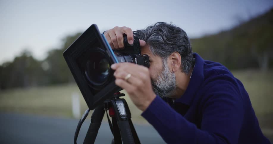 A focused, middle-aged male photographer adjusts his camera on a tripod while shooting outdoors